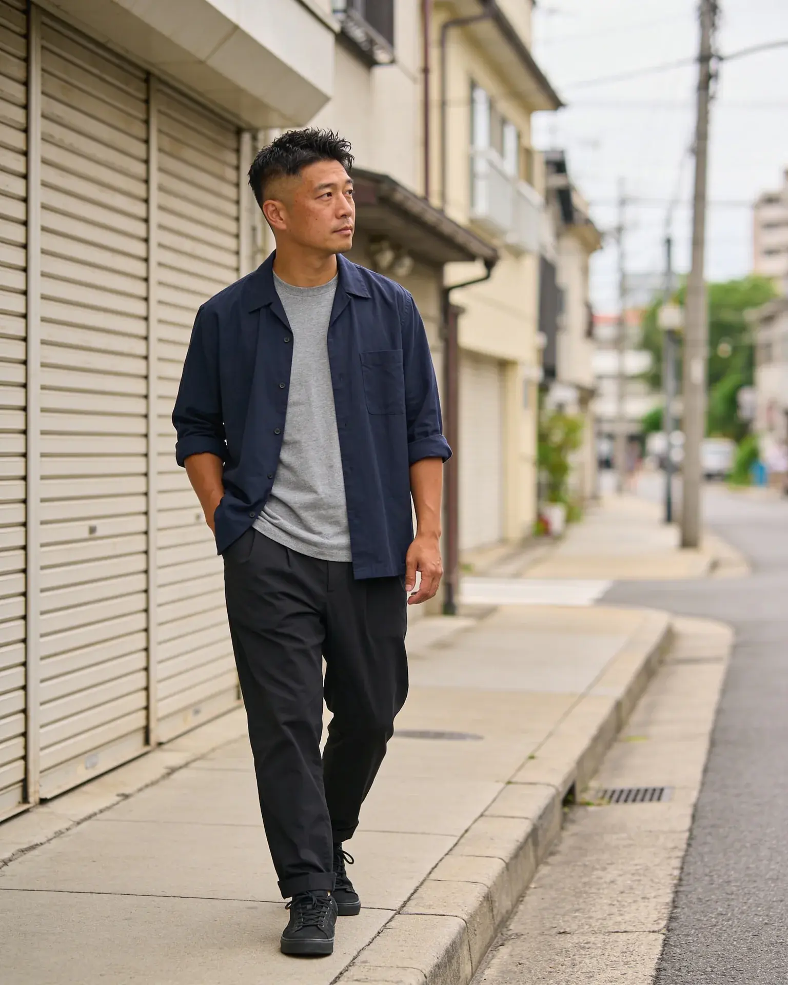 Adult man in a navy overshirt walking on a quiet city sidewalk