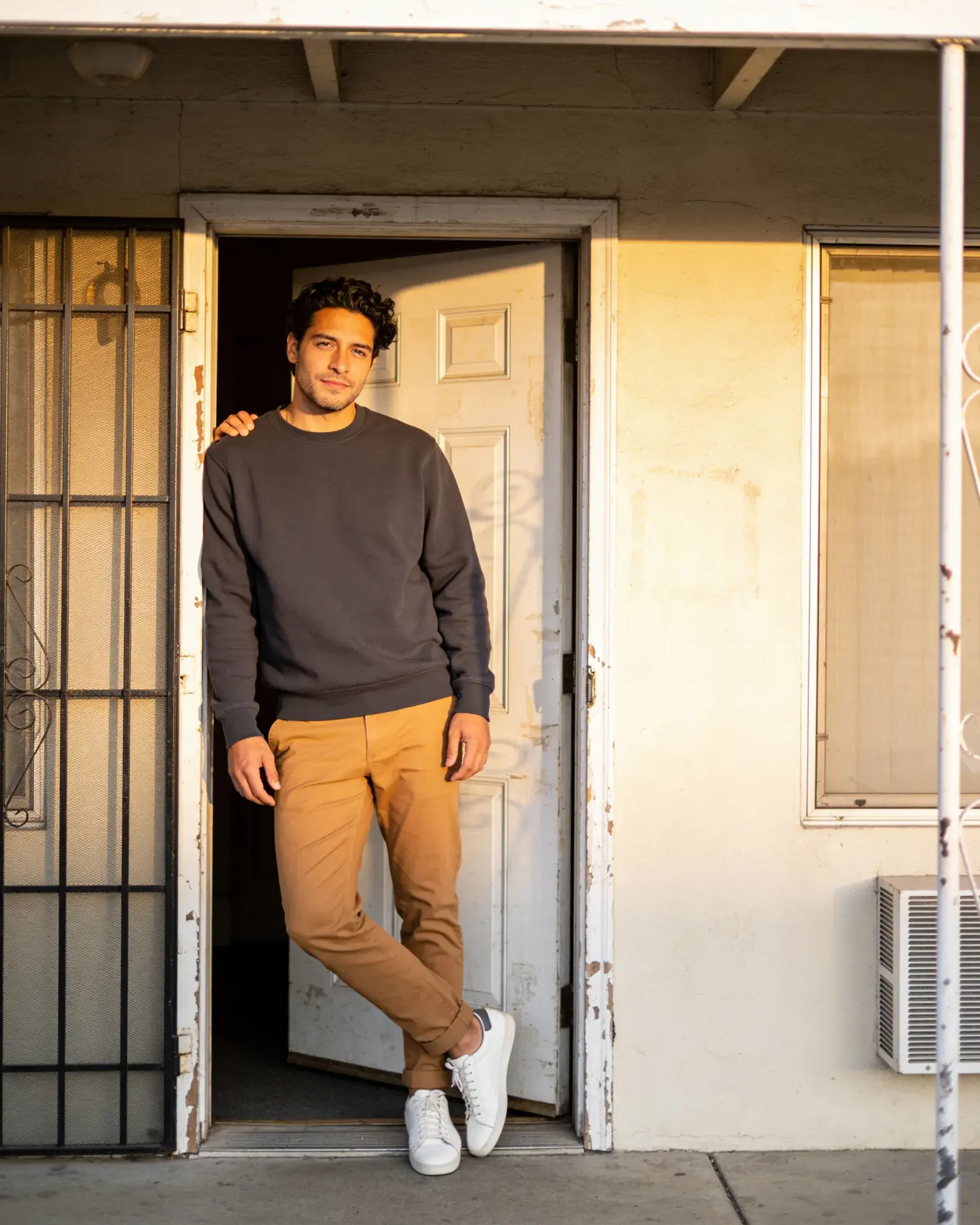 Adult man in a charcoal sweatshirt and tan trousers in an apartment doorway